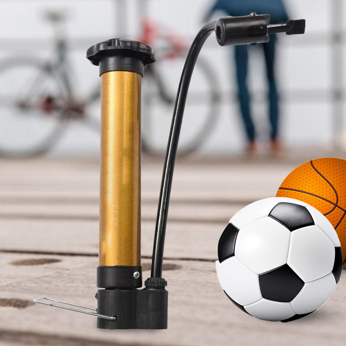 A gold and black hand pump stands next to a soccer ball and a basketball, with a bicycle in the background.