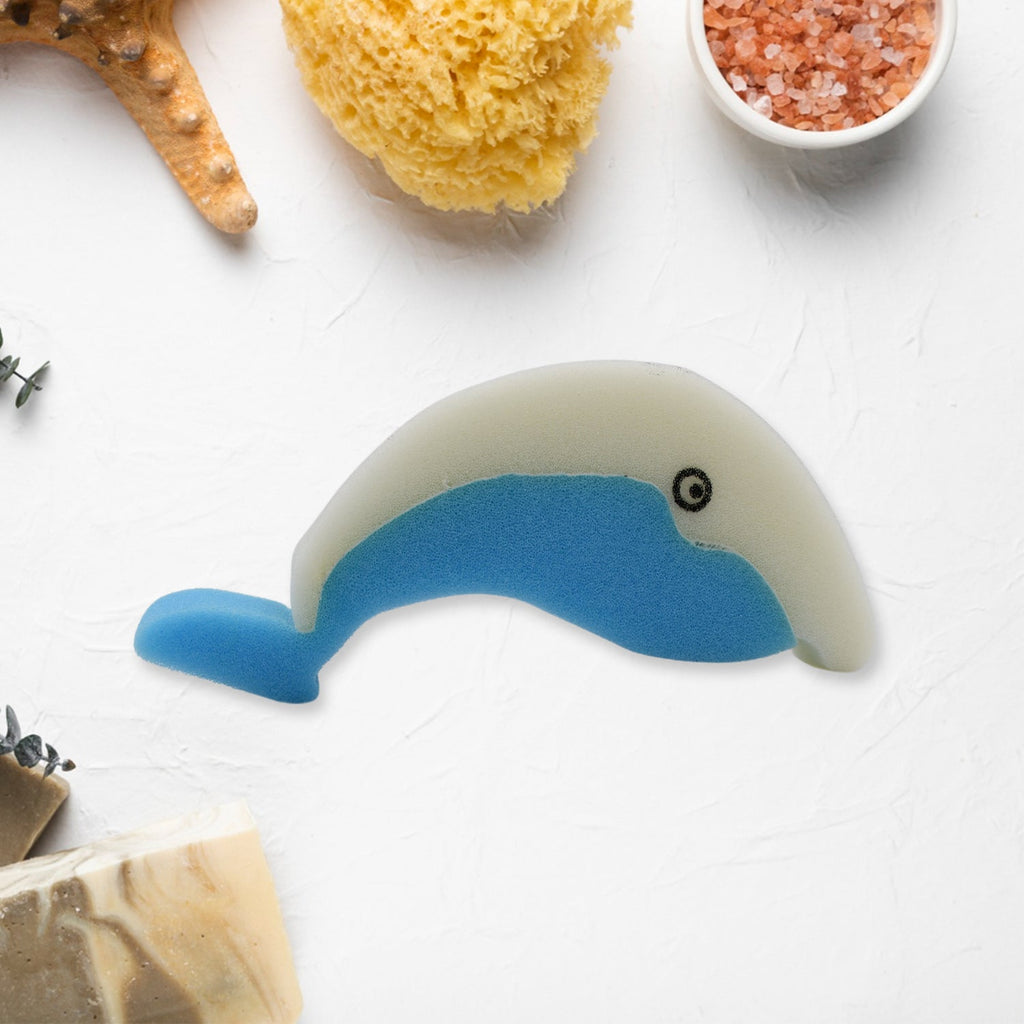 The blue and white dolphin sponge is centered on a white surface surrounded by bath-related items like a loofah and soap.