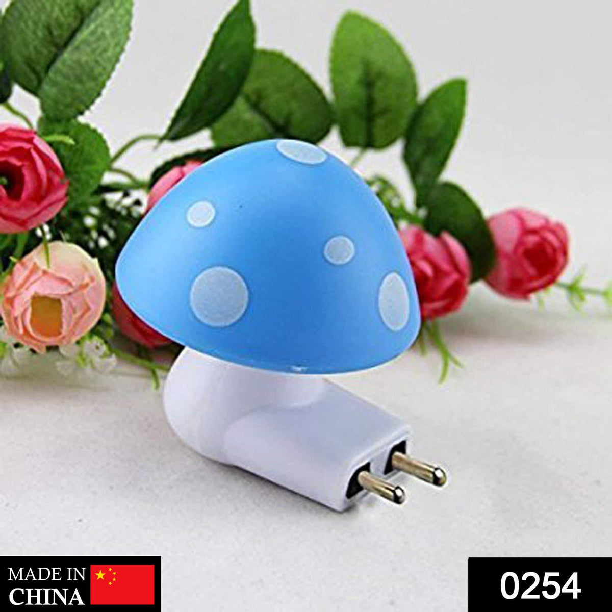 A blue and white mushroom-shaped night light with a two-pin plug is shown against a blurred background of pink flowers.