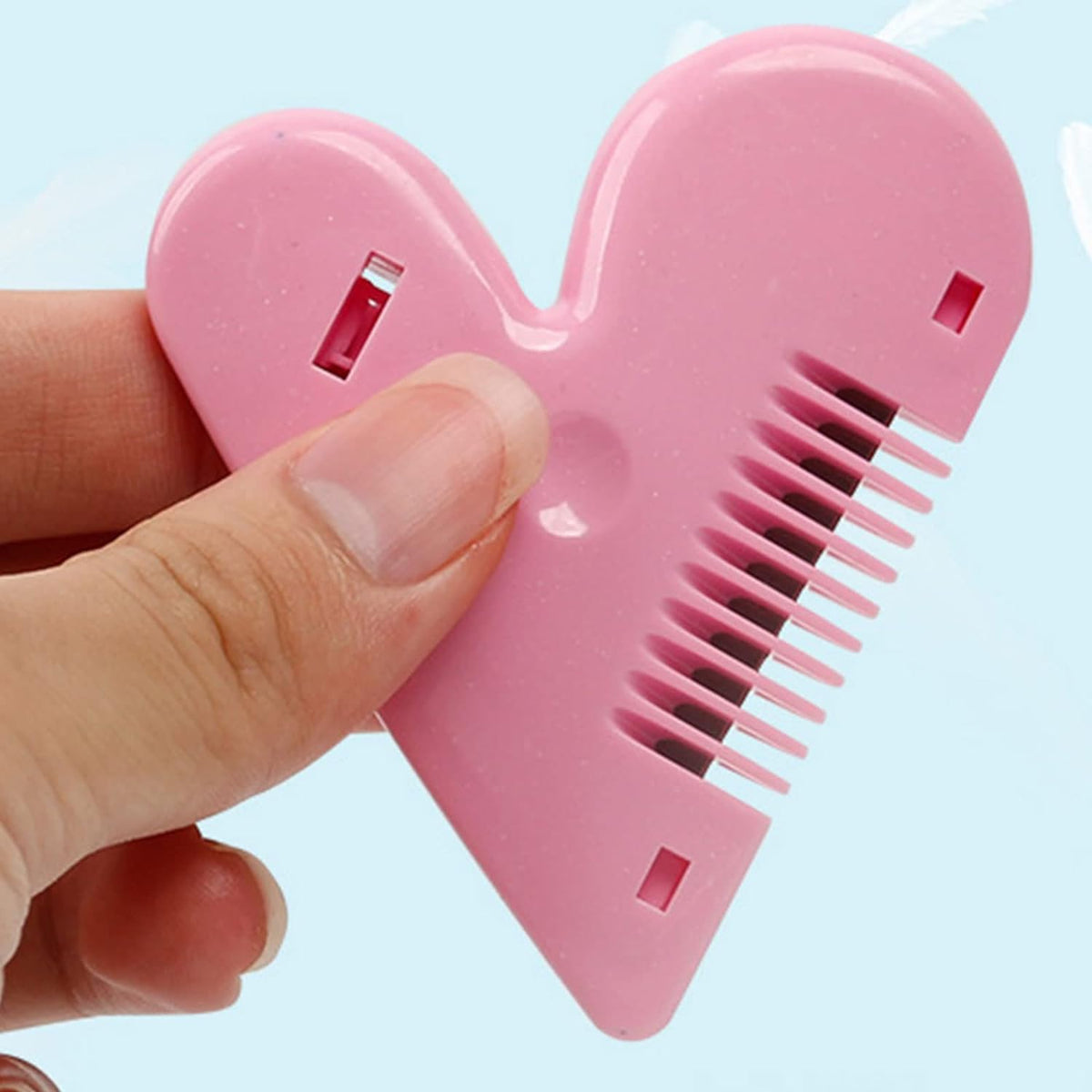 A hand holds a pink heart-shaped hair thinning razor comb, showing its ergonomic design.