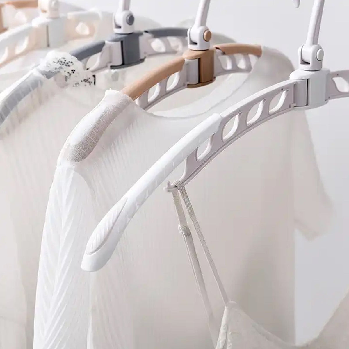 Close-up of a white folding hanger holding a white ribbed shirt, with other hangers in the background.