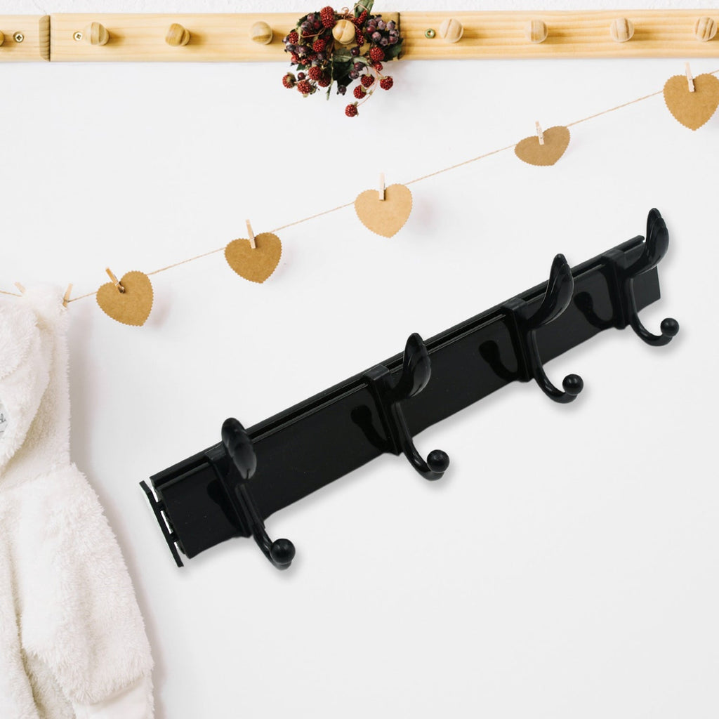 Black four-hook coat rack on a white wall, with heart-shaped paper cutouts on a string and a white robe.