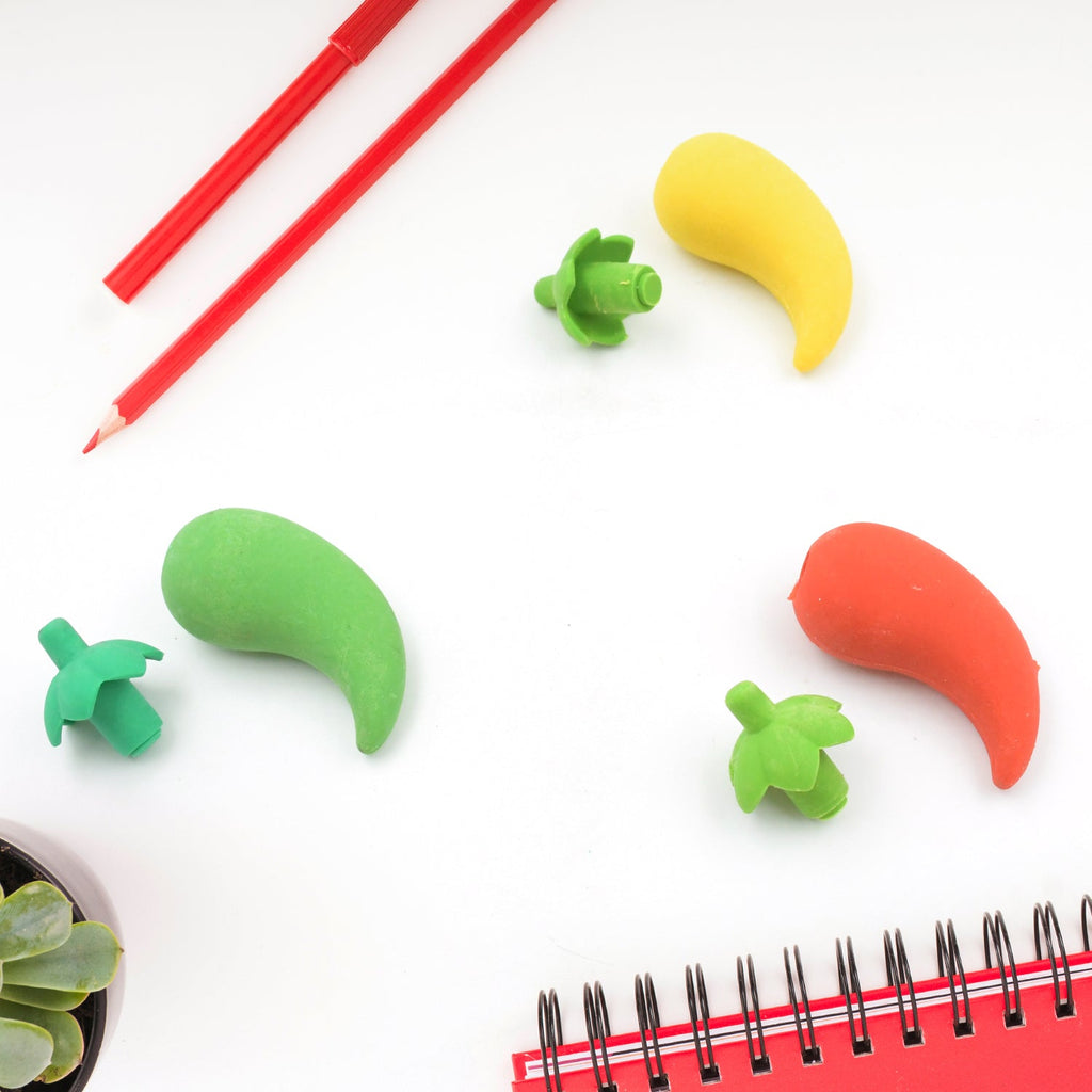Three chili pepper erasers in red, yellow, and green, with their green stems detached, alongside red pencils and a succulent