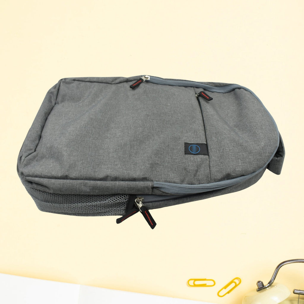 A grey backpack with multiple zippers and a mesh side pocket is shown on a light yellow background.