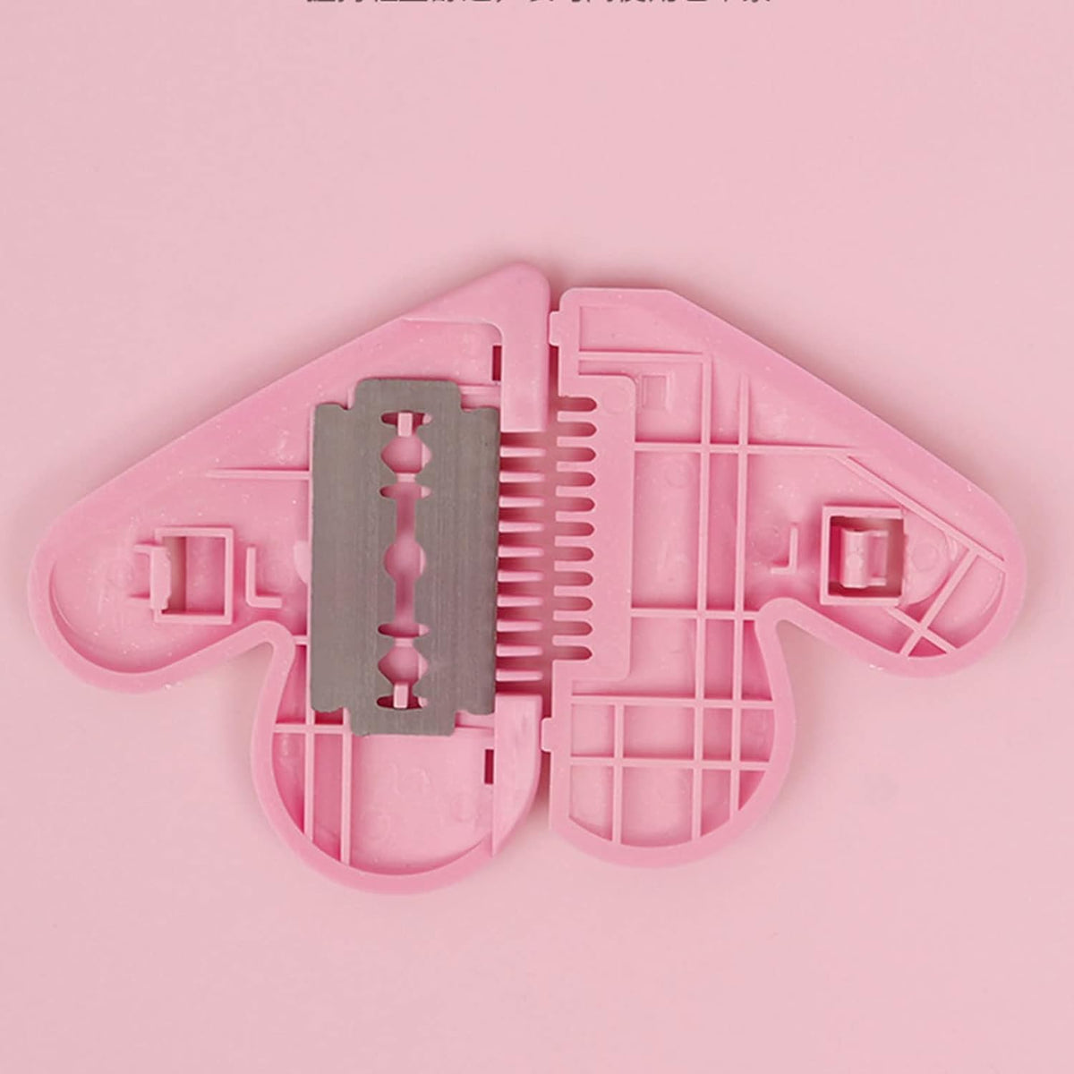 The pink heart-shaped razor comb is open, revealing a double-edged razor blade inside.