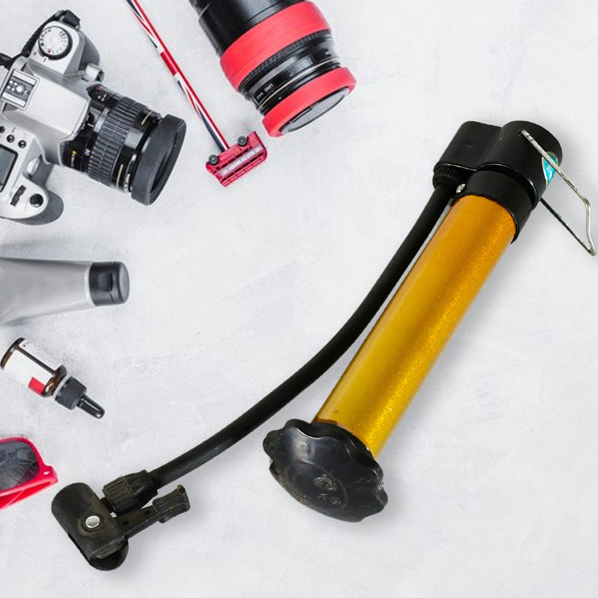 A gold and black hand pump is shown amidst various photography equipment on a light grey surface.