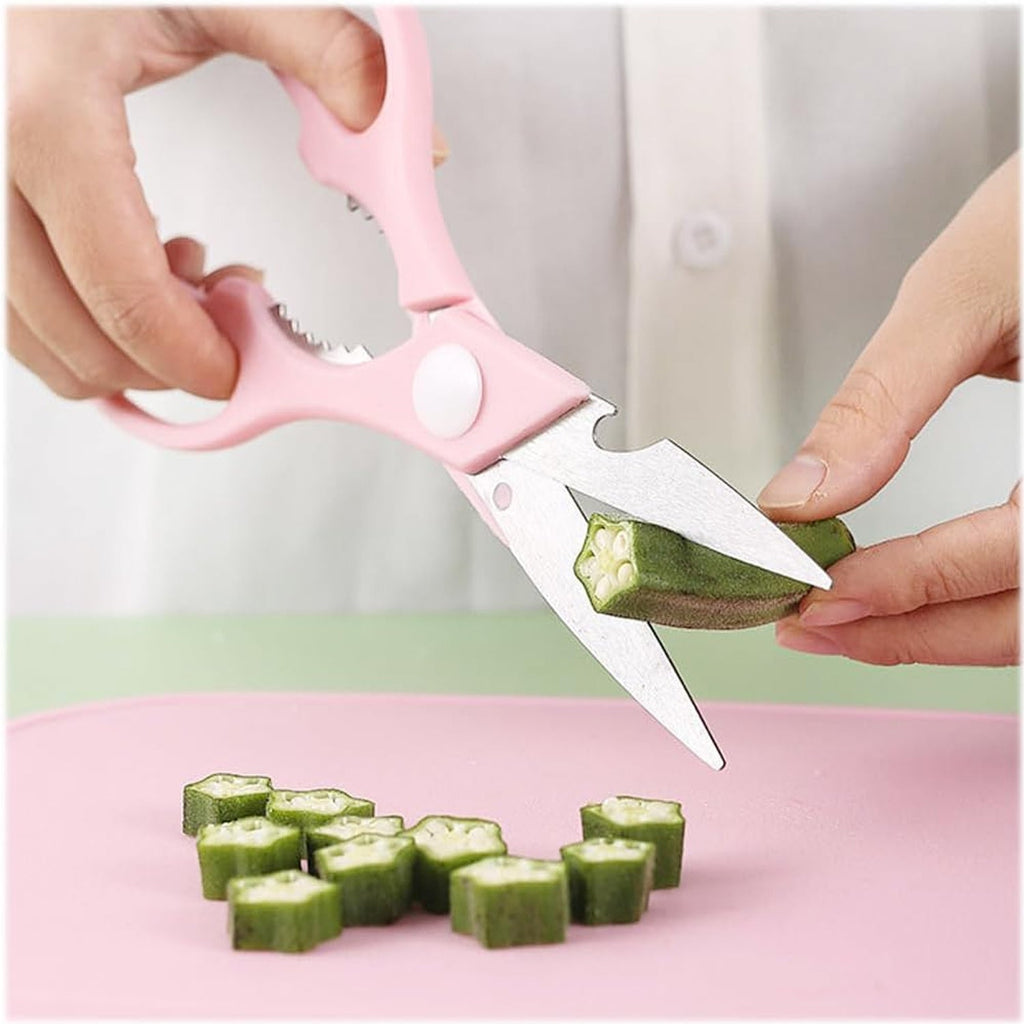 Hands use pink kitchen scissors to cut green okra into small pieces on a pink cutting board.