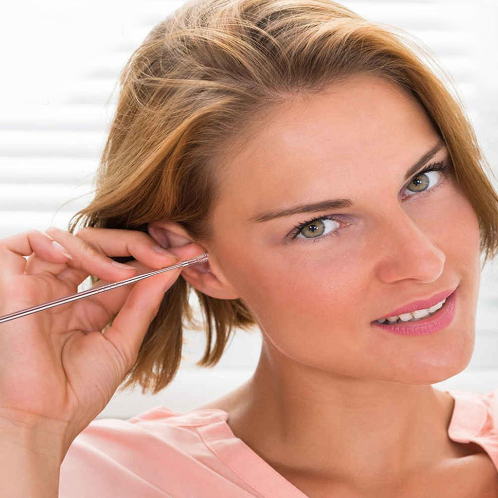 A smiling woman with short hair is using a silver ear cleaning tool on her right ear.