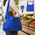 A person carries a blue reusable shopping bag filled with groceries in a supermarket aisle. A small inset shows the bag