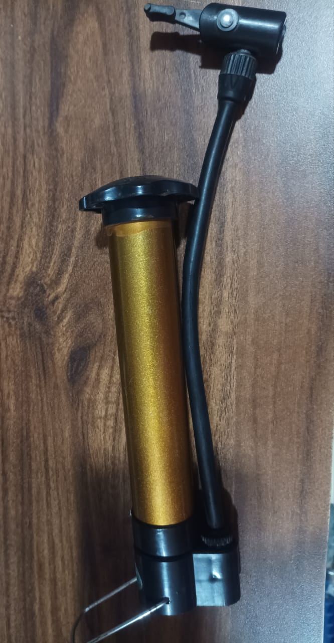 A gold and black hand pump with a black hose and nozzle rests on a wooden surface.