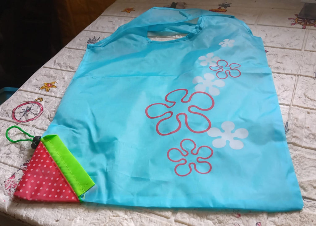 A light blue reusable shopping bag with red and white flower designs lies on a patterned white and brown surface.