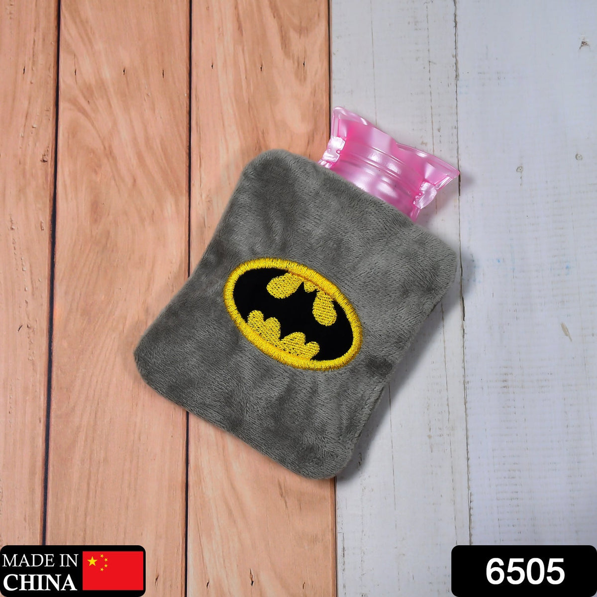 Gray plush hot water bag with a yellow and black Batman logo on a two-tone wooden surface.