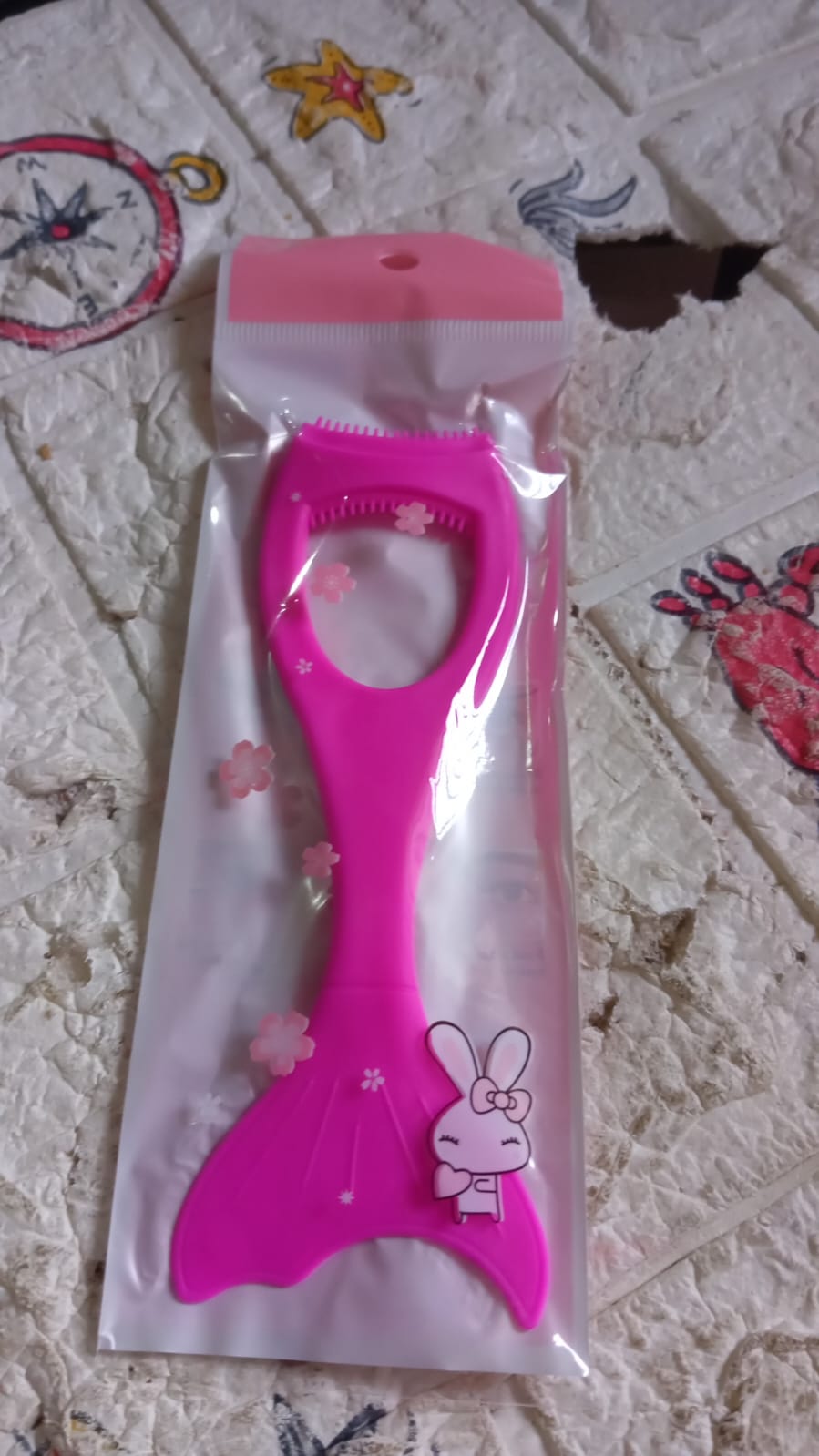 A pink silicone eyeliner guide with a bunny sticker is packaged in clear plastic on a textured background with star and