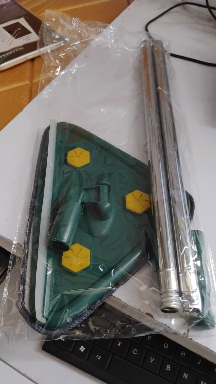The green triangle mop head and its silver handle are packaged in clear plastic, resting on a white surface next to a