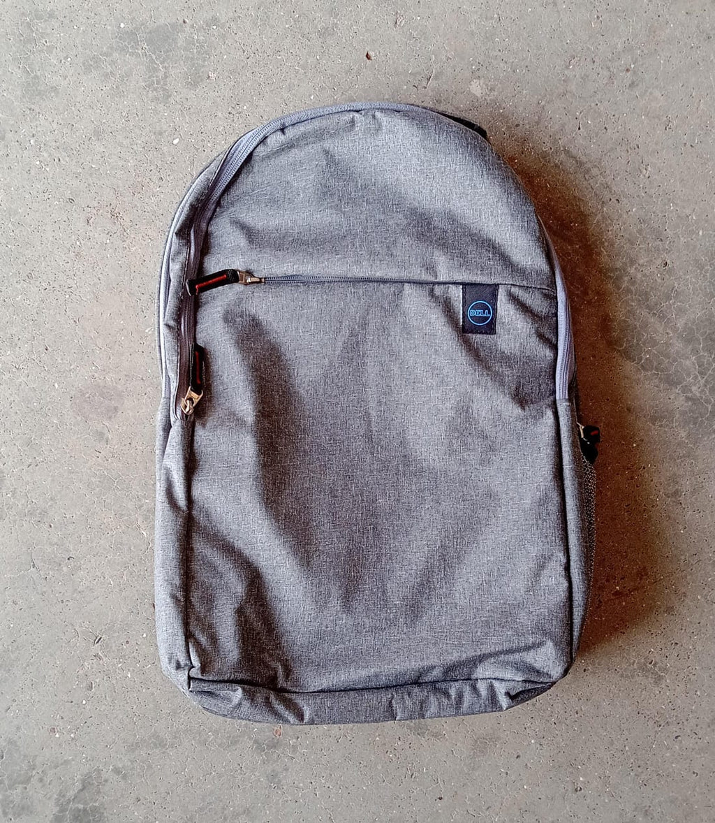 A grey backpack with a front zipper pocket and blue trim lies flat on a textured grey concrete surface.