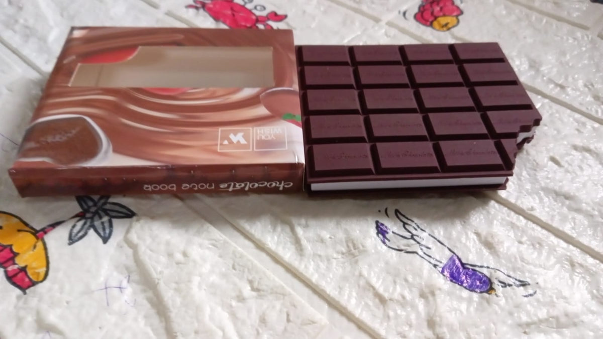 A chocolate bar shaped notebook next to its packaging on a patterned surface.