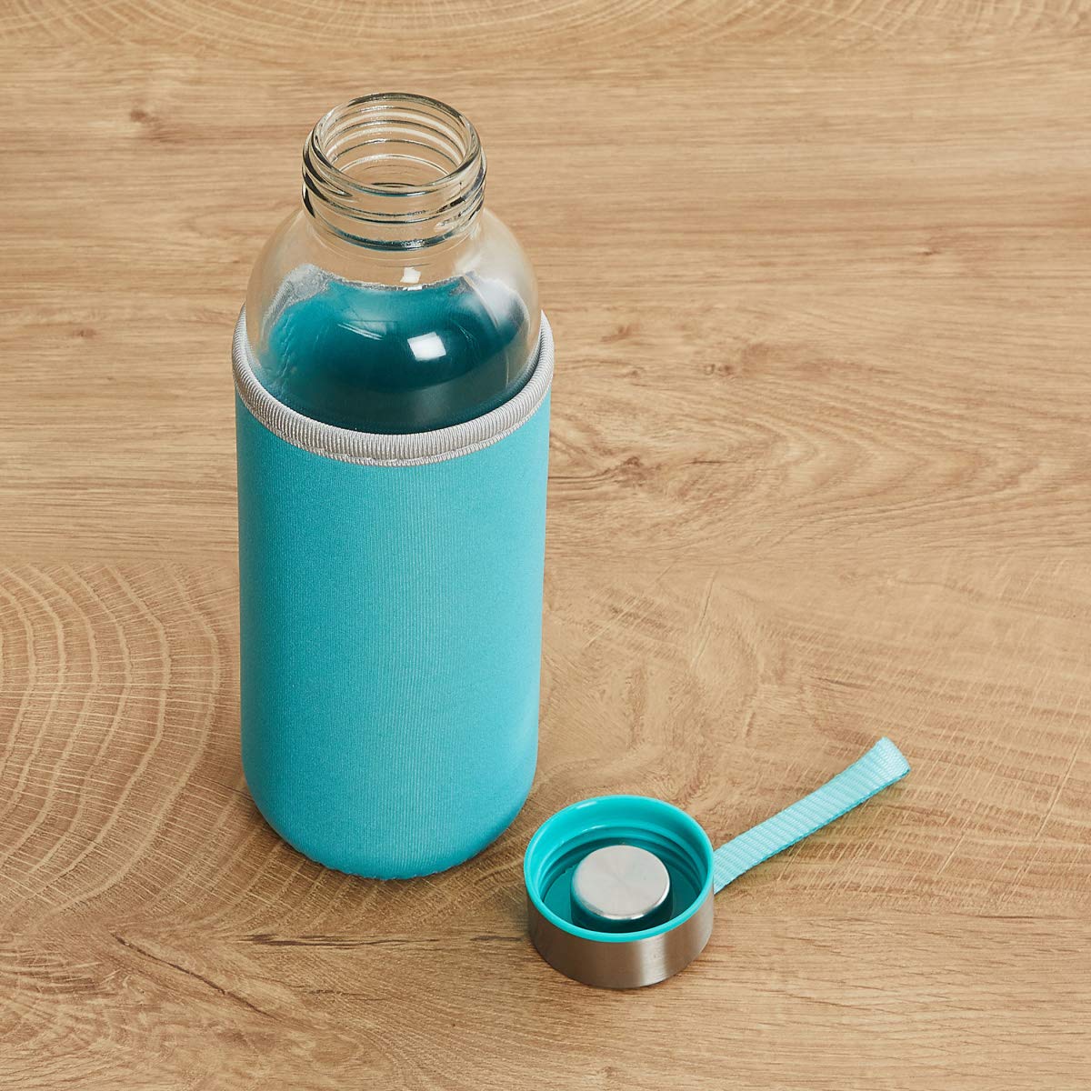A clear glass bottle with a turquoise sleeve and matching lid, placed on a light wooden surface.