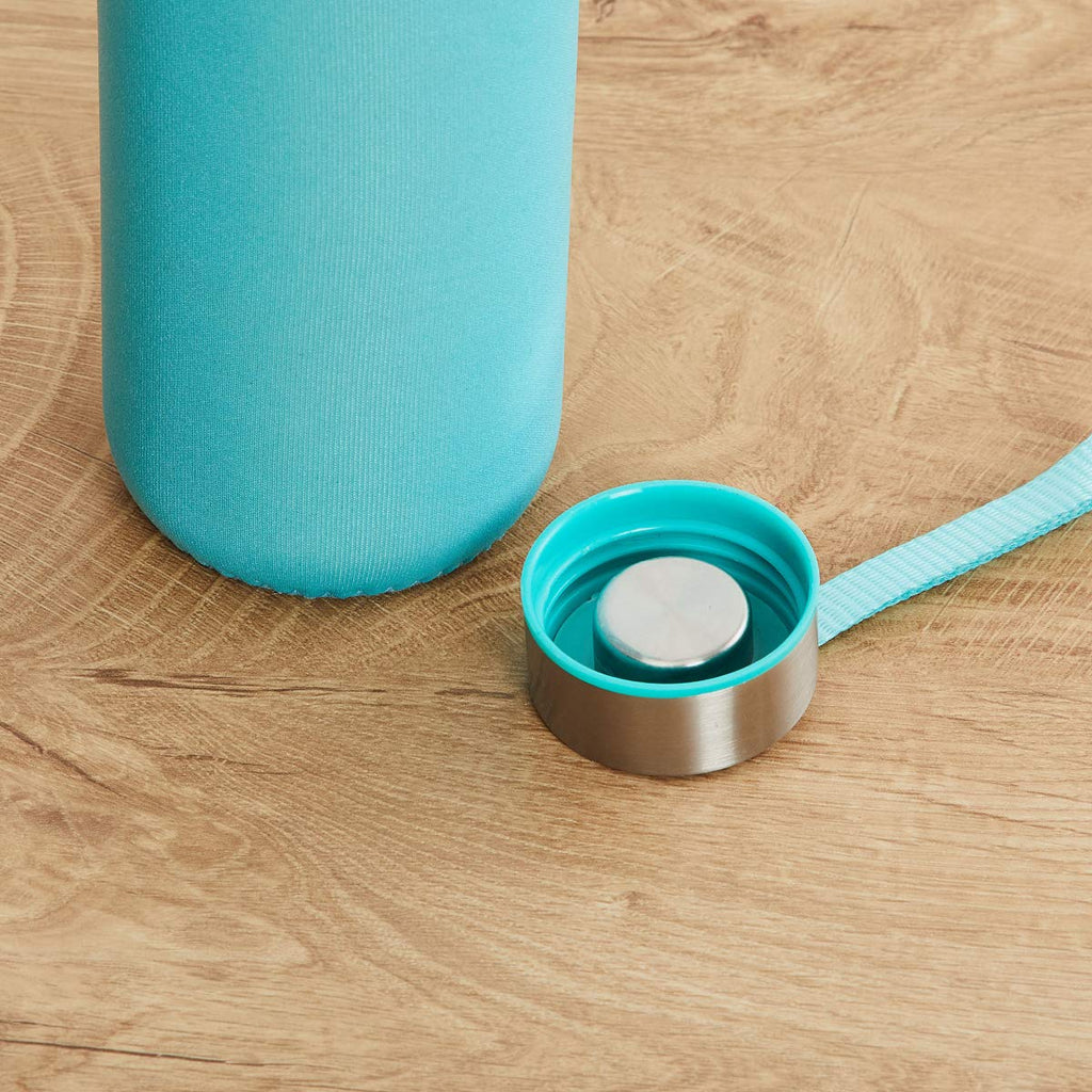 Close-up of the turquoise lid with a silver top, next to the bottle's turquoise sleeve on wood.