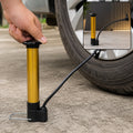 A hand operates a gold and black hand pump to inflate a car tire, with an inset showing the pump alone