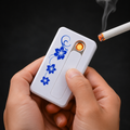 Hands hold a white USB lighter with blue floral pattern, igniting a cigarette with a glowing orange coil.