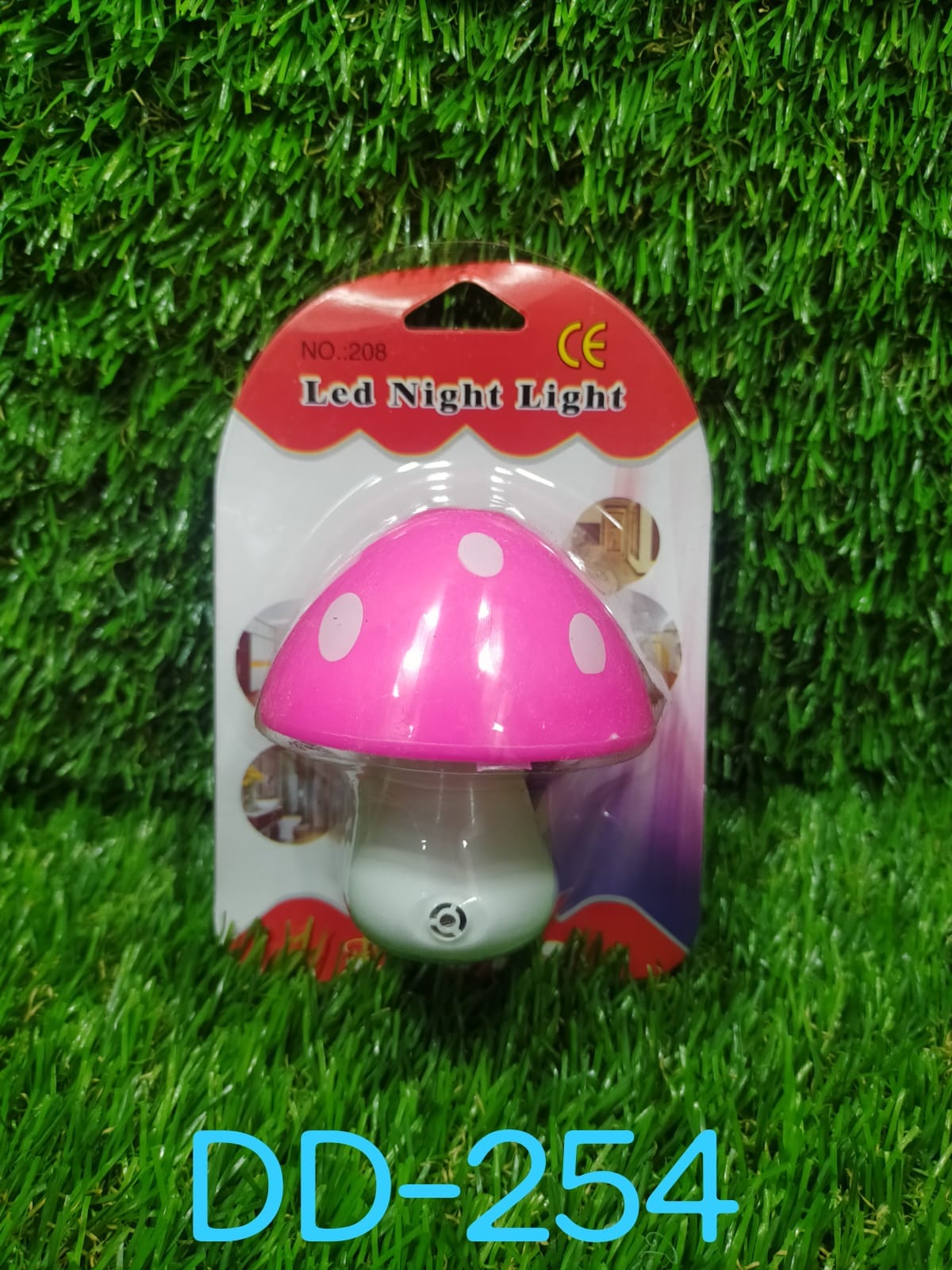 A pink and white mushroom-shaped LED night light in its packaging, displayed on a vibrant green artificial grass background.