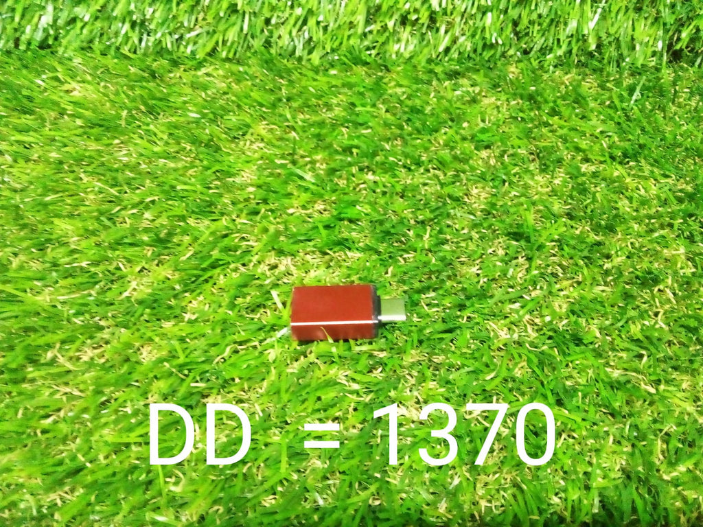A small red USB-C to USB 3.0 OTG adapter is centered on a vibrant green artificial grass background.