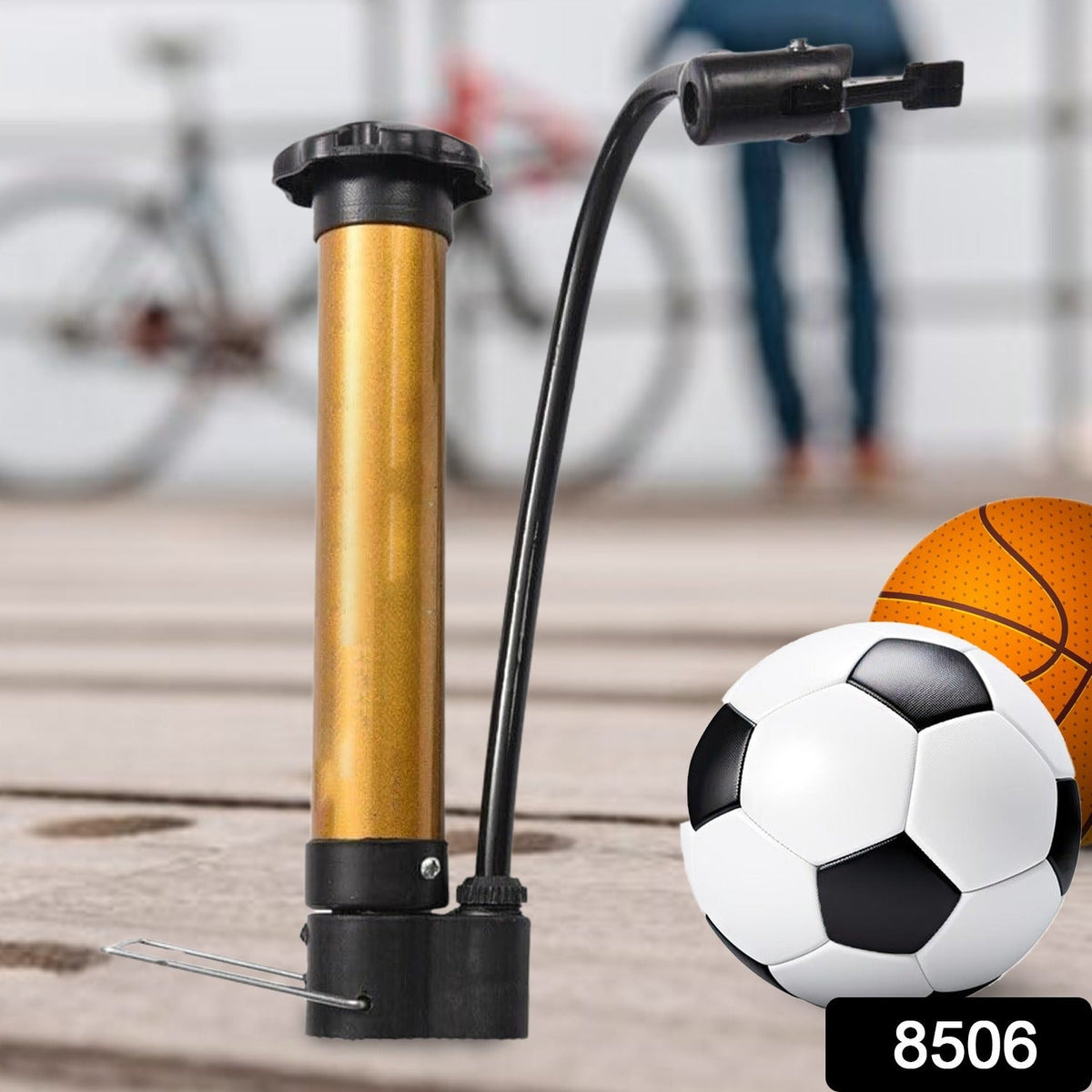 A gold and black hand pump stands next to a soccer ball and a basketball, with a bicycle in the background